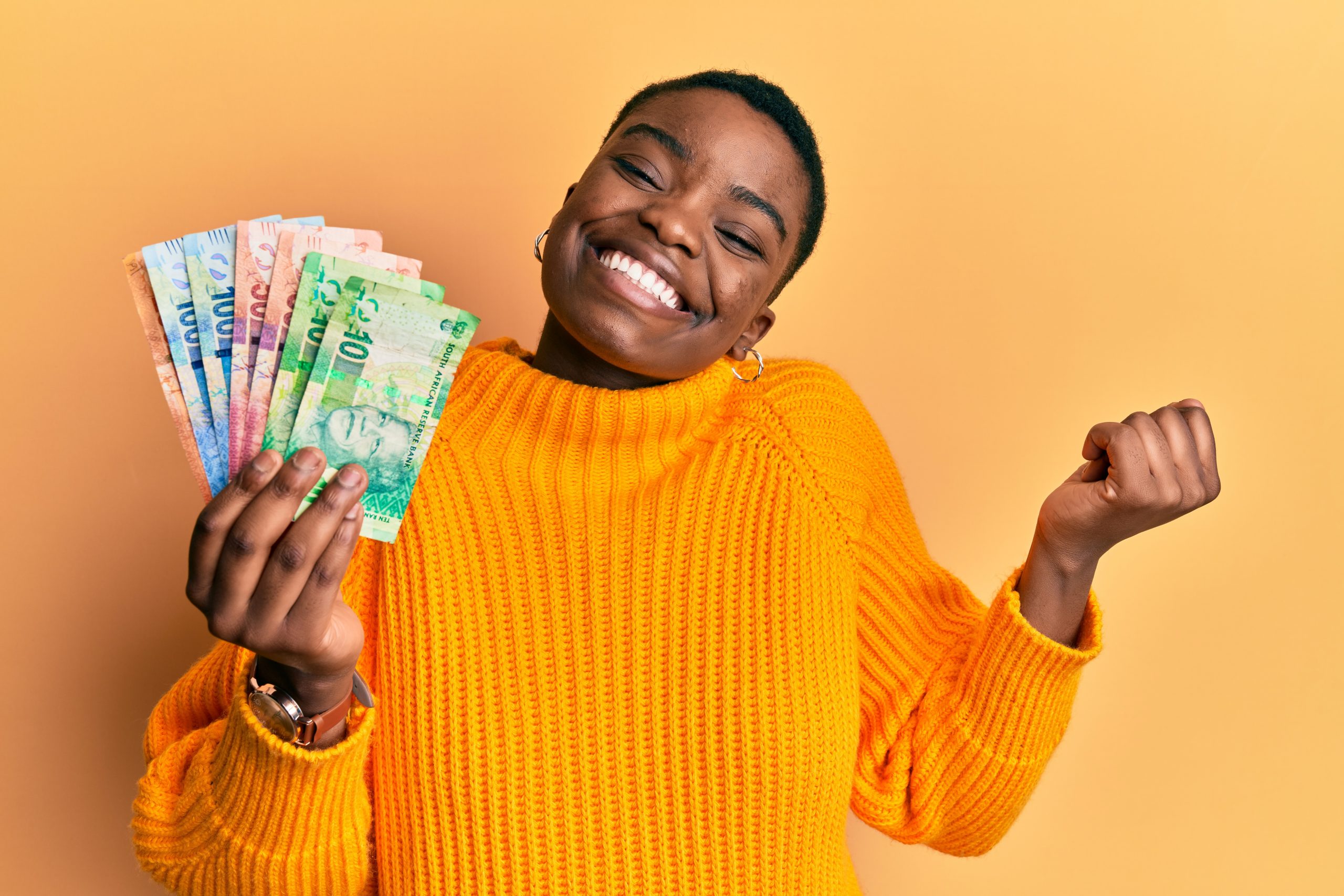 Young african american woman holding south african rand banknotes screaming proud, celebrating victory and success very excited with raised arm