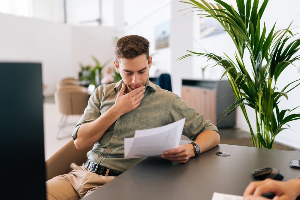 Portrait of focused male client reading contract for real estate property purchase. Thoughtful man reading terms of conditions of document, making decision
